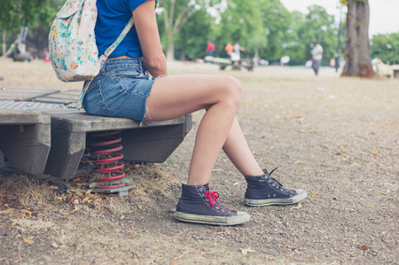 A young woman is sitting on some playground equipment with springs outside in summerの写真素材