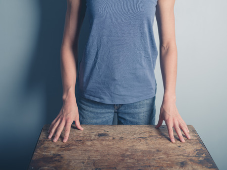 A young woman wearing a blue vest is standing behind an old deskの写真素材