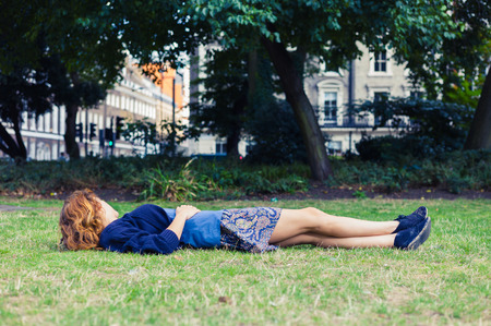 A young woman is lying on the grass in a park in the cityの写真素材