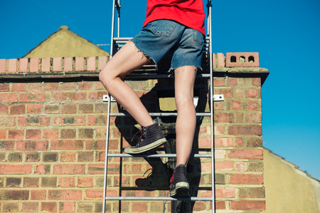 A young woman is climbing a ladder on a roofの写真素材