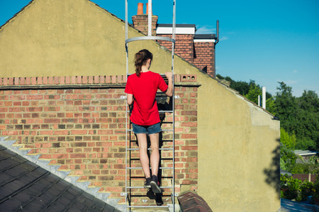 A young woman is climbing a ladder on a roofの写真素材