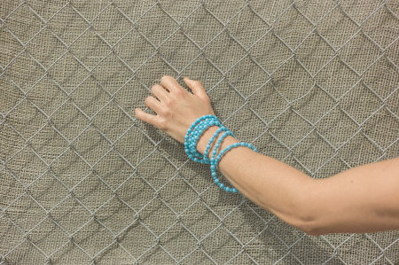The hand of a young woman wearing a blue bracelet is grabbing a fence outsideの写真素材