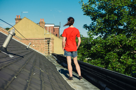 A young woman is standing on a roof on a sunny dayの写真素材