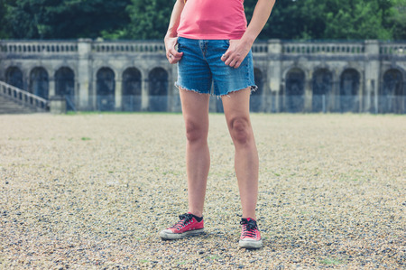 A young woman is standing in a grand formal garden with ornamental features in the backgroundの写真素材