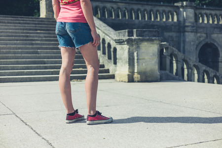 A young woman is standing near the steps of an old Victorian building outside in a park or grand formal gardenの写真素材