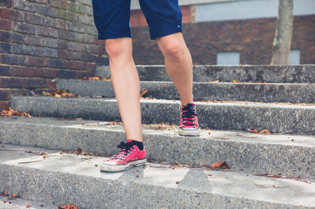 The legs of a young woman wearing shorts as she is walking down some steps outside