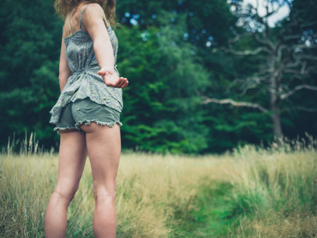 A young woman is standing in a meadow in the forest on a sunny summer day and is offering a helping handの写真素材