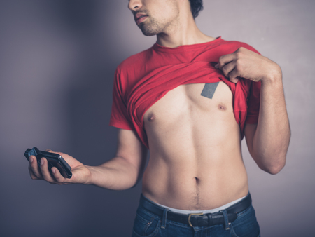 A fit young man is lifting up his shirt to take a selfie of his toned bodyの写真素材