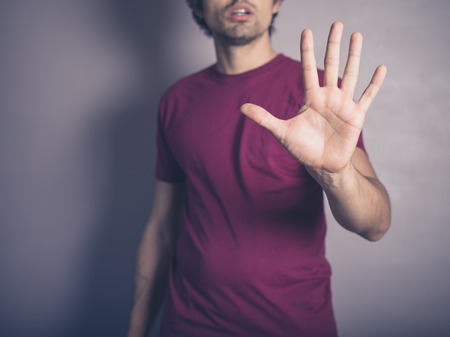 A young man wearing purple is raising his open hand to signal stopの写真素材