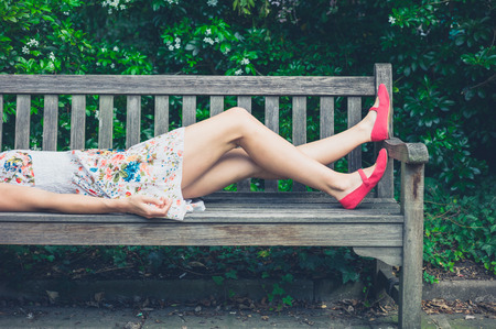 A young woman wearing a summer dress is relaxing on a bench in the park on a sunny dayの写真素材