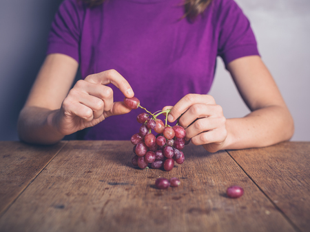 A young woman is sitting at a table and eating grapesの写真素材