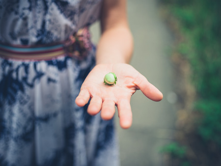 A young woman is displaying a green hazelnut she has found in the forestの写真素材