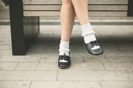 The feet of a young woman as she is sitting on a bench in the cityの写真素材