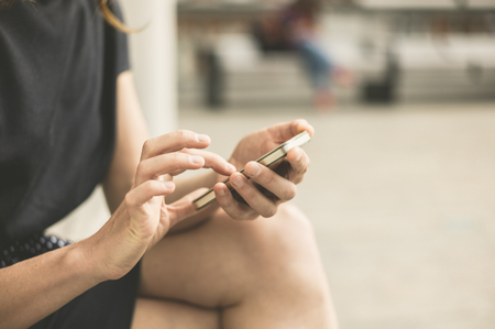 A stylish young woman is sitting outside in the city and is using her smart phoneの写真素材