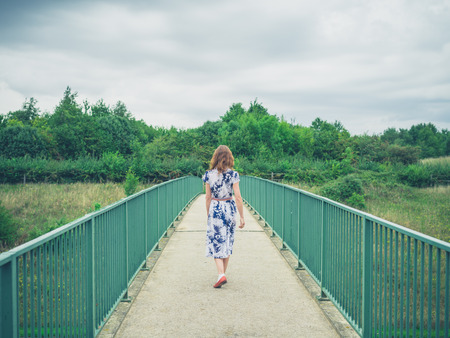 A young woman wearing a dress is crossing a footbridge in a rural settingの写真素材
