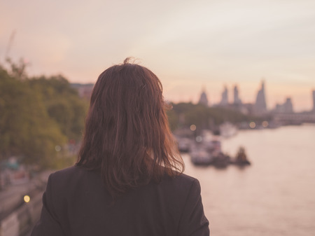 A young businesswoman is standing on a bridge at sunrise and is admiring the London skylineの写真素材