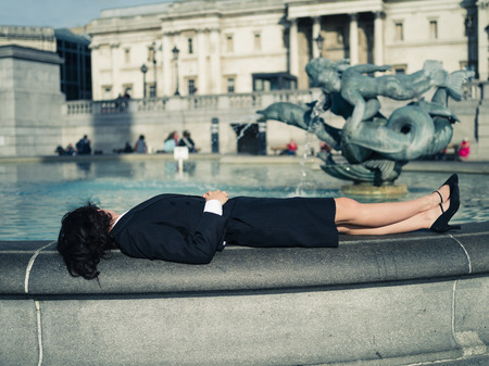 A young businesswoman is lying by a fountain and relaxing on a sunny day in the cityの写真素材