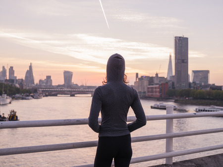 A young woman wearing a sporty hoodie is standing on a bridge in London at sunriseの写真素材