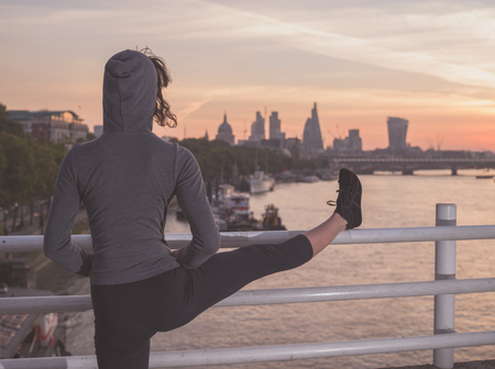 A young fitness woman is stretching her leg on a bridge in London at sunriseの写真素材
