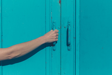 A young female hand is grabbing the handle of a big blue door outsideの写真素材