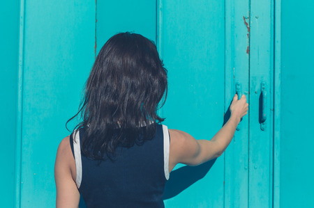A young woman is grabbing the handle of a blue door outsideの写真素材