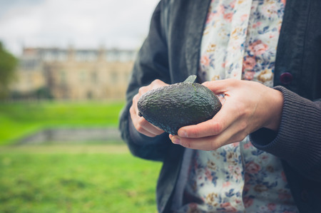 A young woman is cutting an avocado in a garden outsideの写真素材