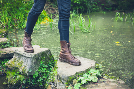 The feet of a young person trekking across stepping stones in a small pond