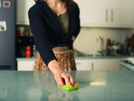 A young woman is scrubbing and cleaning the worktop in her kitchen with a spongeの写真素材