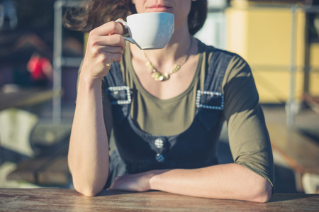 A youngwoman is enjoying a cup of coffee outside a cafe on a sunny dayの写真素材