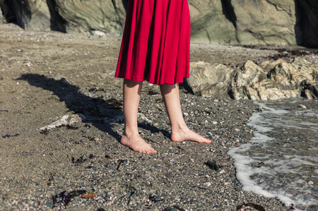 The feet of a young woman in a red dress as she is walking on a beachの写真素材