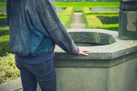A young woman is standing by a well in a formal gardenの写真素材
