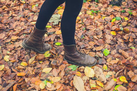 The feet of a young woman wearing boots walking in some leaves in the autumn