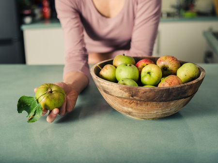 A young woman is holding an apple in a kitchen with a bowl of apples next to herの写真素材