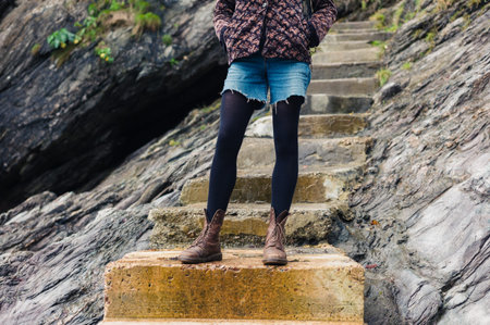 A young woman wearing hiking boots is standing on some concrete steps outdoors amongst the rocks