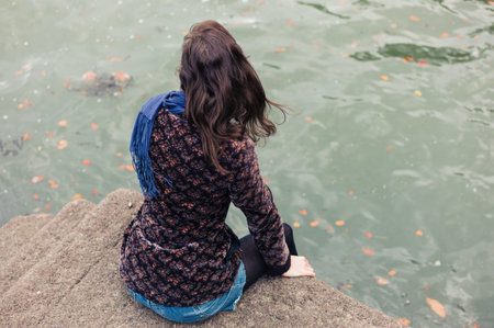 A young woman is sitting on a concrete pier and is admiring the waterの写真素材