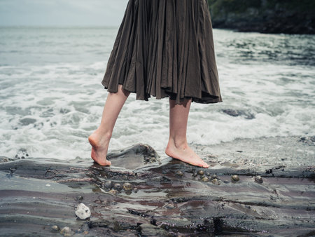 The feet of a young woman as she is walking on some rocks in the water on the shore