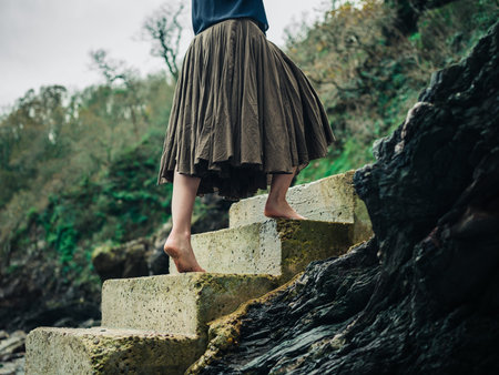 The feet of a young barefoot woman as she is walking up some concrete steps in nature