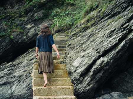 A young barefoot woman is walking on some stairs leading up a cliffの写真素材