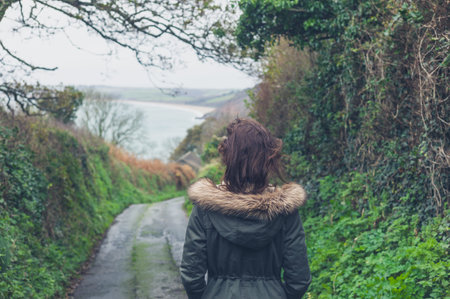 Rear view shot of a young woman walking on a country road by herself in the autumn or winterの写真素材