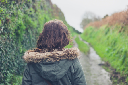 Rear view shot of a young woman walking on a country road by herself in the autumn or winterの写真素材