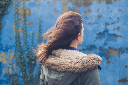 A young woman is standing by a blue wall on a winter day with her hair blowing in the windの写真素材