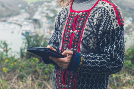 A young woman is standing in nature on an autumn day and is using a tablet