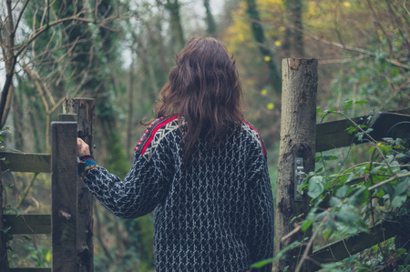 A young woman is opening a gate in the forest on an autumn dayの写真素材