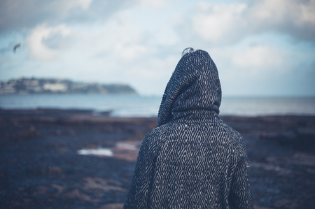 A young woman wearing a hooded coat is walking on a dramatic beach in the winterの写真素材