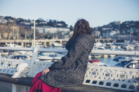 A young woman is sitting and relaxing on the pier in a seaside townの写真素材