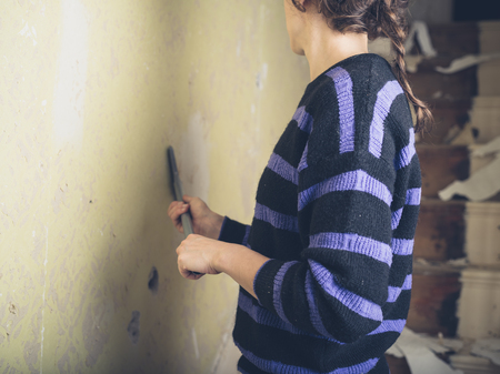 A young woman is renovating a house and is stripping off the wallpaperの写真素材