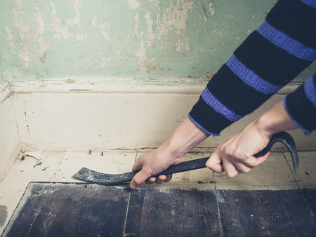 A young woman is prying the nails in her floorboards with a crowbarの写真素材
