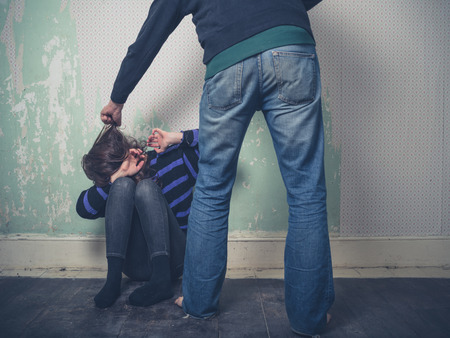 A young woman is sitting on the floor as her partner attacks herの写真素材