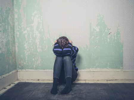 A sad young woman is sitting on the floor in an empty roomの写真素材