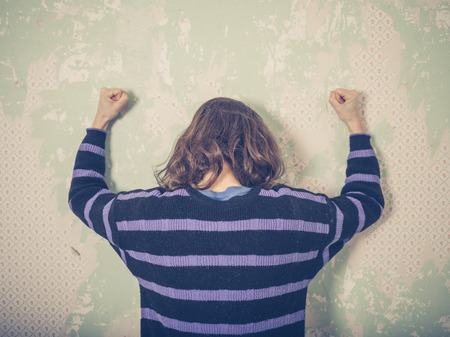 A frustrated young woman is banging her fists against a wallの写真素材